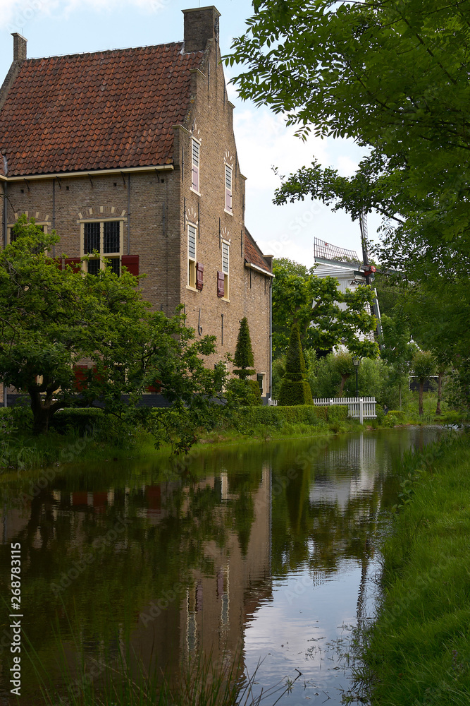 Old traditional Dutch house and mill along a river with reflection in the Netherlands Old traditional Dutch house and mill along a river with reflection in the Netherlands