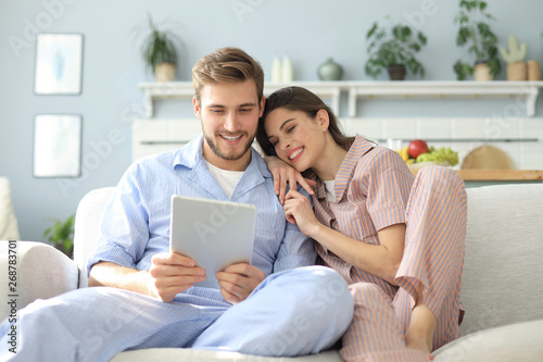 Young couple watching media content online in a tablet sitting on a sofa in the living room.