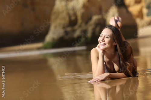 Happy girl in bikini dreaming lying on the beach