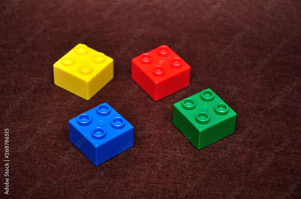 Four small building blocks of different colors on a brown background Four small building blocks of different colors on a brown background
