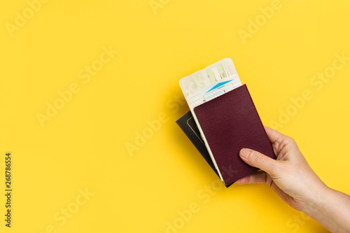 Mano de mujer sosteniendo un pasaporte y billete de viaje sobre un fondo amarillo liso y aislado. Vista de frente y de cerca. Copy space photo