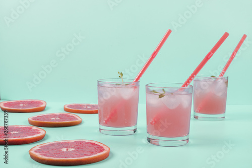 Three glasses of cold grapefruit juice and slices over the mint backdrop