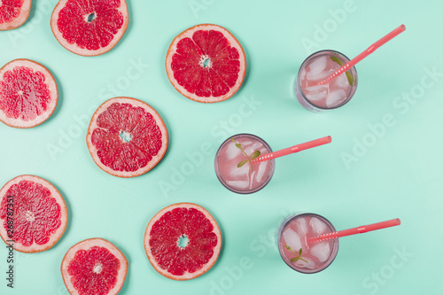 An overhead view of grapefruits slices and glass of juice with ice and mint on pastel background