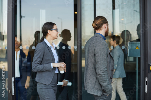 Group of modern business people in formal outfits coming in convention center through revolving door