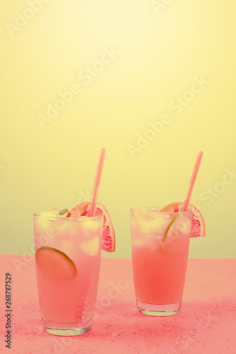 Fresh pink alcoholic cocktail with grapefruit; lemon slice and ice cubes against yellow background
