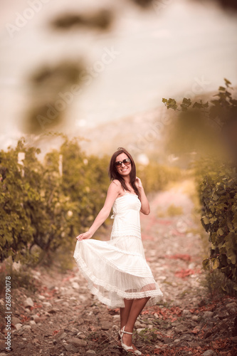 Smiling woman in white dress standing in vineyard