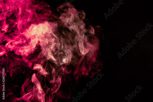 Beautiful column of smoke in the neon bright light of red, green, pink and turquoise on a black background exhaled out of the vape. Nice pattern for printing and backdrop of colored waves.