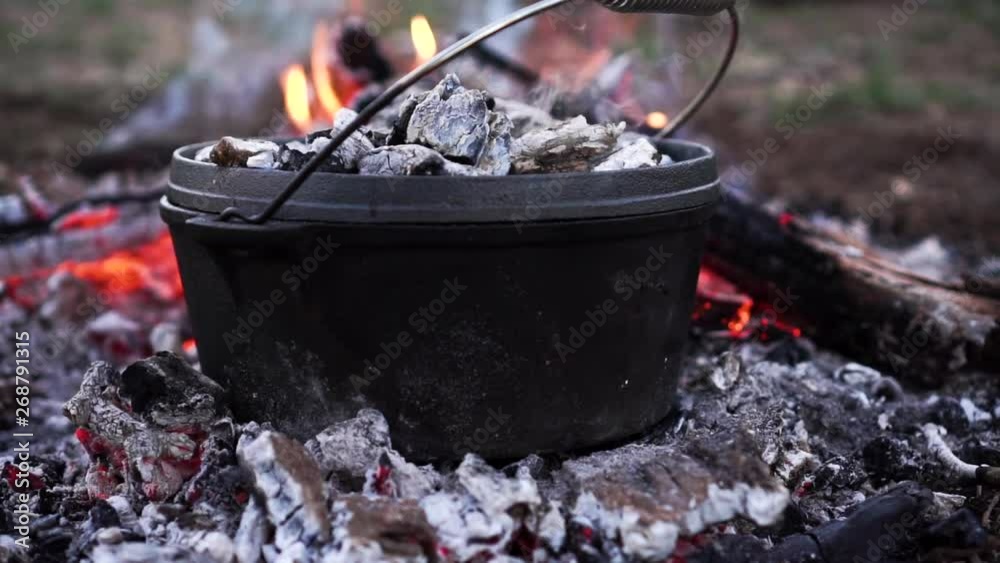 Orbiting around a black cast iron pot sitting on red hot coals on an open fire at dusk
