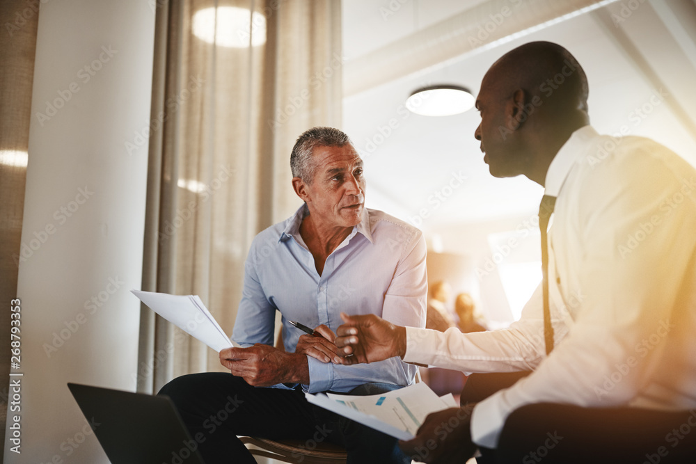 Two diverse businessmen going over documents together in an offi Two diverse businessmen going over documents together in an offi