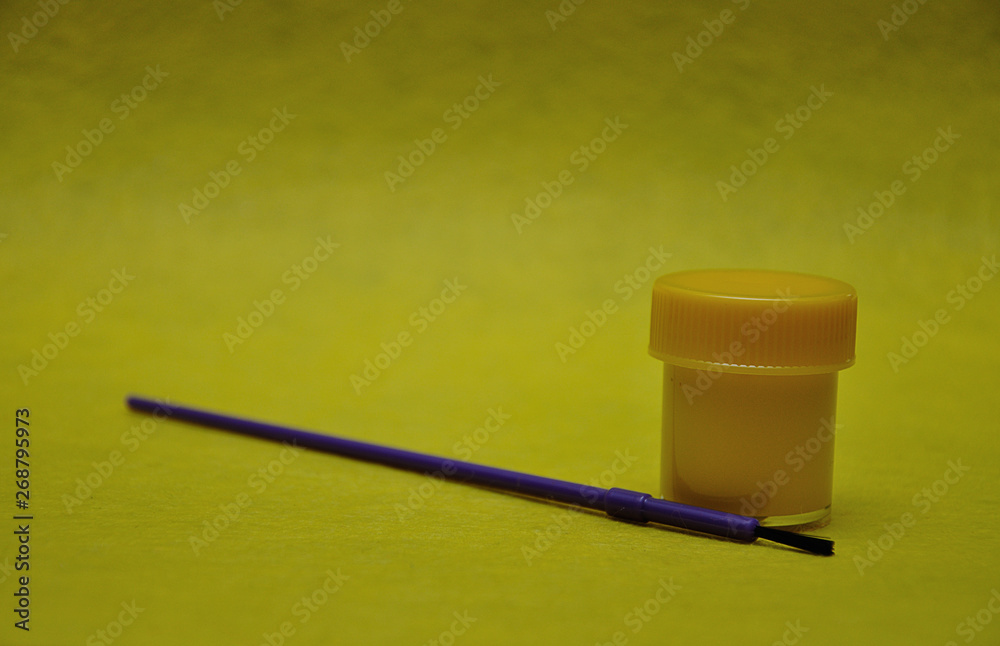 Fototapeta premium A pot of yellow paint with a purple paintbrush on a yellow background