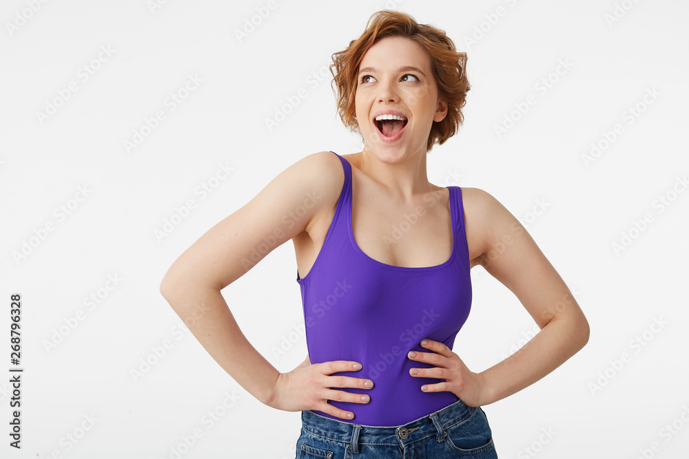 Photo of young happy surprised attractive short-haired girl, wearing a purple jersey, looking up with open eyes and mouth isolated over white wall with copy space. Photo of young happy surprised attractive short-haired girl, wearing a purple jersey, looking up with open eyes and mouth isolated over white wall with copy space.