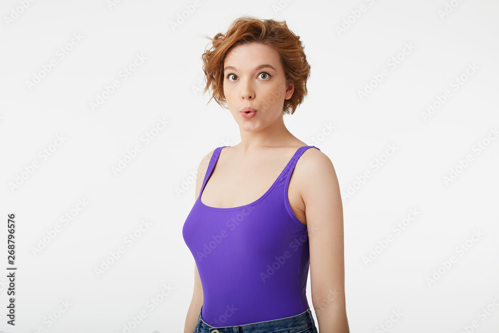 Photo of amazed young attractive short-haired girl, wearing a purple jersey, amazed looking up at the copy space, speaks lips Photo of amazed young attractive short-haired girl, wearing a purple jersey, amazed looking up at the copy space, speaks lips