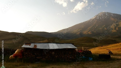 A panning shot of an old wooden cottage on foothill of Damavand's mountain A shot of an old cottage in extended field on foothill of Damavand mountain during summer sunlight clouds moving in sky