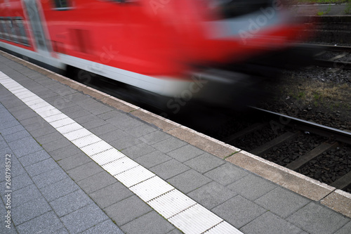 Die weiße Linie markiert den Sicherheitsabstand zur Bahnsteigkante am Bahnsteig und einfahrender Nahverkehrszug - Stockfoto
