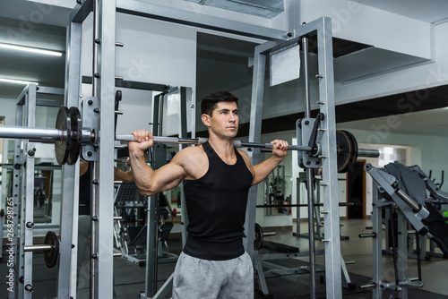 Young man lifting up barbell in gym