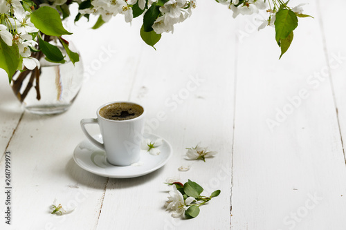Spring still life. Cup of coffee with apple tree flowers and petals of flowers are on white cafe table outside in blooming garden