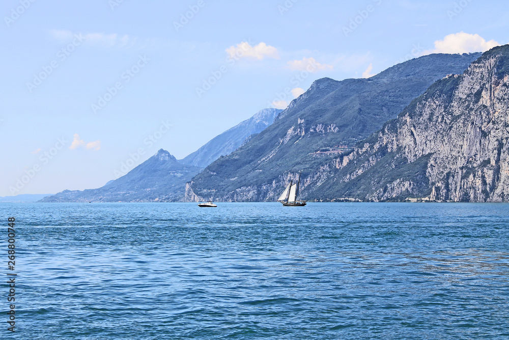 Summer landscape on lake Garda Italy with turquoise water white yacht and green mountains on the banks