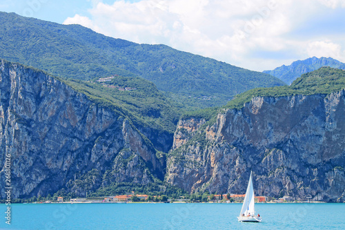 Summer landscape on lake Garda Italy with turquoise water white yacht and green mountains on the banks