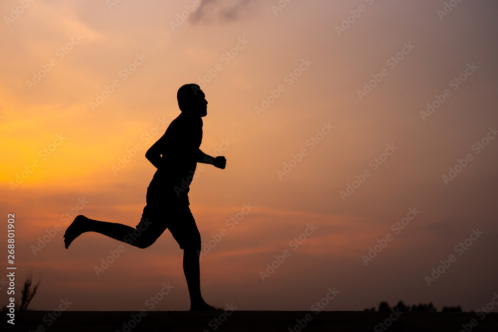 Fototapeta premium Man running alone at beautiful sunset in the road at park . Summer sport and freedom concept. Athlete training on dusk. - Image