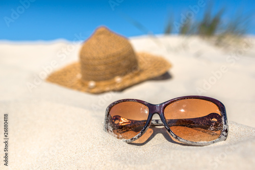 Background with summer vacation accessories on the beach, sunglasses and sun hat on sand dune and blue sky.