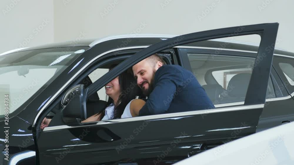 A man pulls out a girl from a new car in the showroom A man pulls out a girl from a new car in the showroom