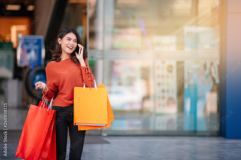 Portrait of a happy Asian pretty girl holding shopping bags while using smartphone in shopping mall background concept. Portrait of a happy Asian pretty girl holding shopping bags while using smartphone in shopping mall background concept.