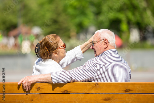 Senior couple wearing sunlglasses relaxing sitting on a bench in city park