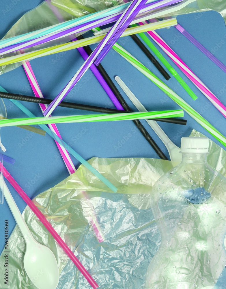 The concept of pollution environment. Cellophane bag, plastic bottle, disposable forks and spoons, cocktail tubes on blue background. Top view