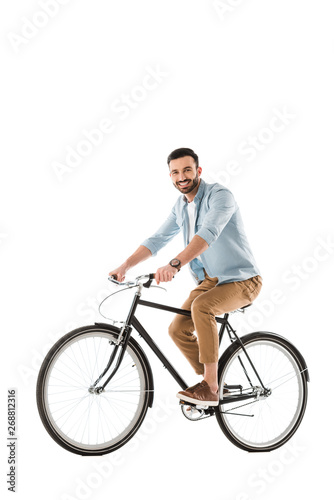 cheerful bearded man riding bicycle and smiling at camera isolated on white