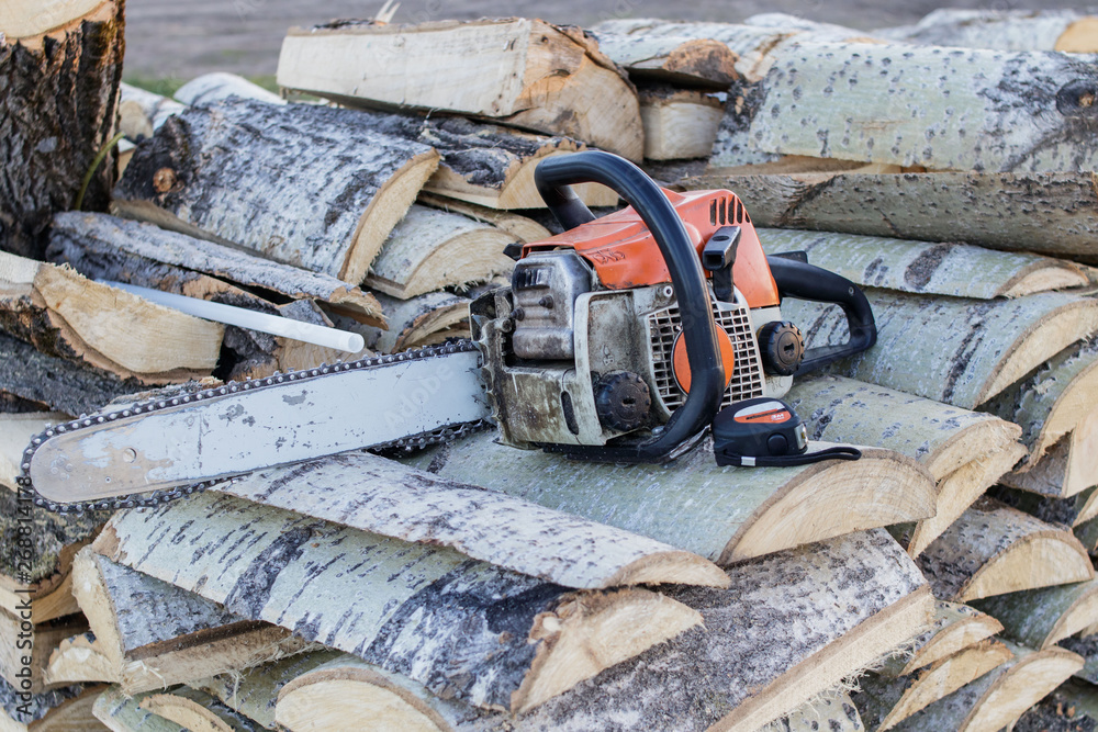 Old chainsaw and tape measure lying on a woodpile of aspen firewood.