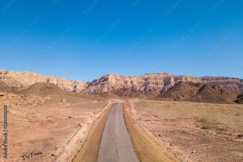 Long stretch of an old Desert road with mountains and blue sky in the background, Aerial image.