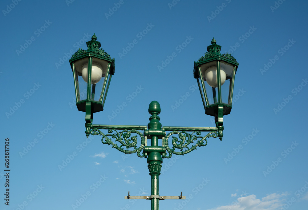 Retro vintage lamp and lantern is made of cast iron. Historical illumination on the street during sunny daylight, clear blue sky in the background.