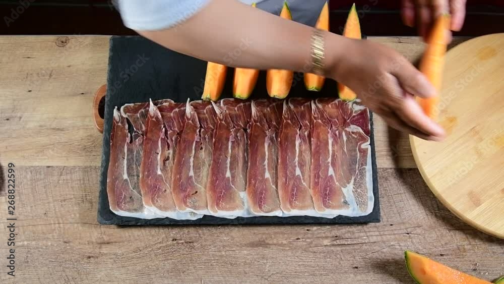 Concept of mediterranean food with melon and ham. Woman preparing on  blackboard, ham and melon,  on a wooden table. Slow motion