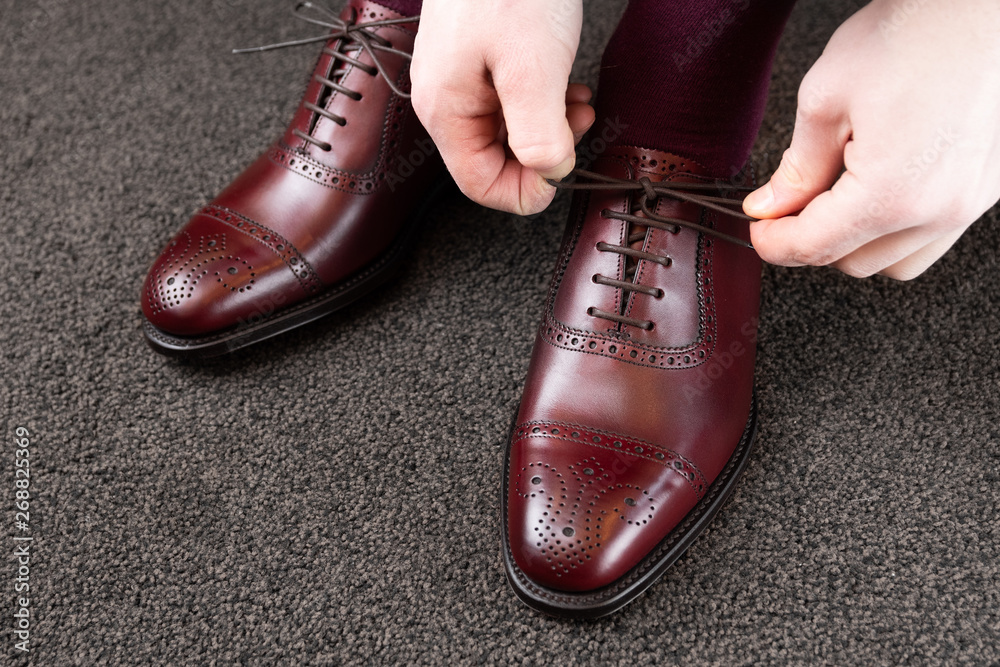 Trying new shoes. Man is putting on a new pair of luxury burgundy full grain leather shoes at footwear store