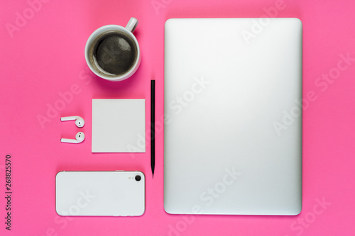 Laptop Phone Coffee Cup on Pink Background Flatlay with Copy Space. White Smartphone, Earphone and Pencil on Minimal Clear Layout Workplace with Paper Note. Business Workspace Inspiration Concept