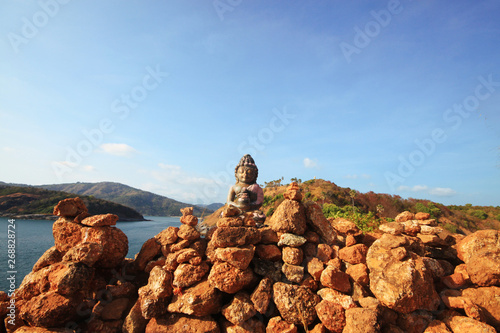 Beautiful Pyramid shape of stones arranged with Buddha statue in zen on rock mountain in seascape of sunset and sea horizon with Dry grass field on Phrom Thep Cape in Phuket island, Thailand.