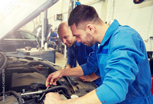 auto service, repair, maintenance and people concept - mechanic men with wrench repairing car at workshop