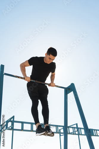 Photo of energetic guy doing acrobatics on horizontal gymnastic bar during morning workout by seaside