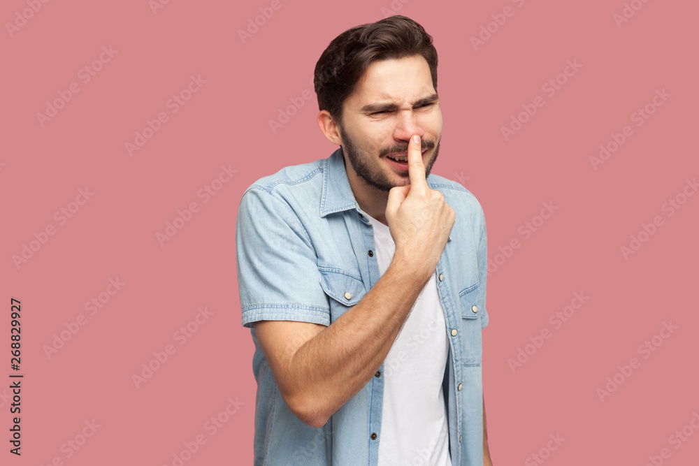 You are liar. Portrait of angry handsome bearded young man in blue casual style shirt standing, touching his nose and showing lie gesture. indoor studio shot, isolated on pink background.