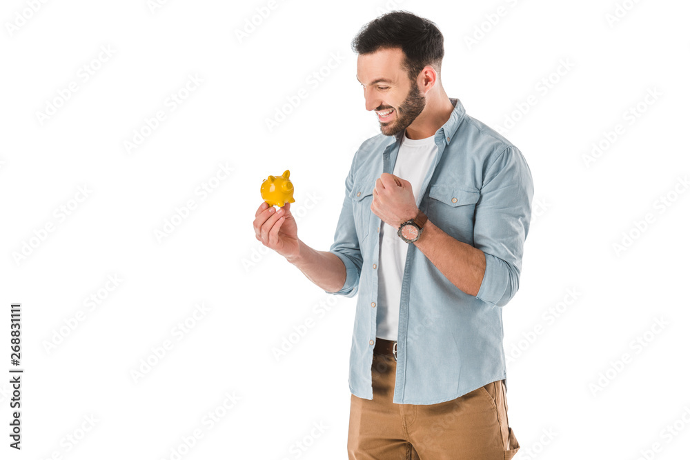happy handsome man looking at piggy bank and smiling isolated on white