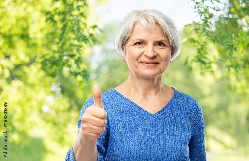 gesture and old people concept - portrait of smiling senior woman in blue sweater showing thumbs up over green natural background gesture and old people concept - portrait of smiling senior woman in blue sweater showing thumbs up over green natural background
