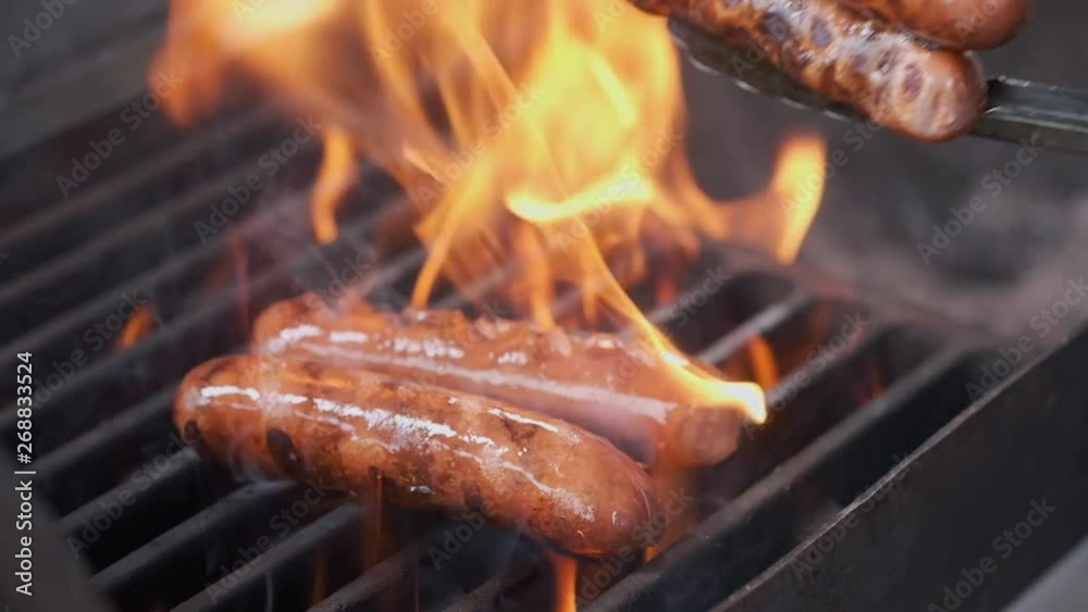 Tasty juicy sausages grilling over a fire. Cook man preparing sausages on the grill. Throws on the grill and flips over. Family summer vacation. Slow motion.
