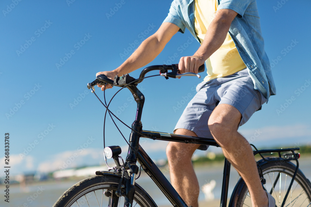 people, leisure and lifestyle concept - close up of young man riding bicycle along summer beach