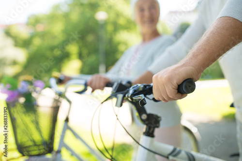 old age, people and lifestyle concept - close up of senior couple with bicycles at park in summer