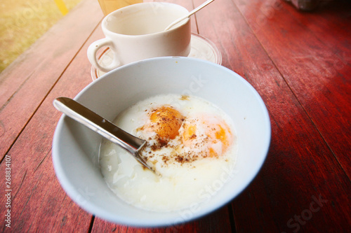 hot coffee with Rice porridge, egg and pork on white bowl on wood table. Breakfast in Thailand