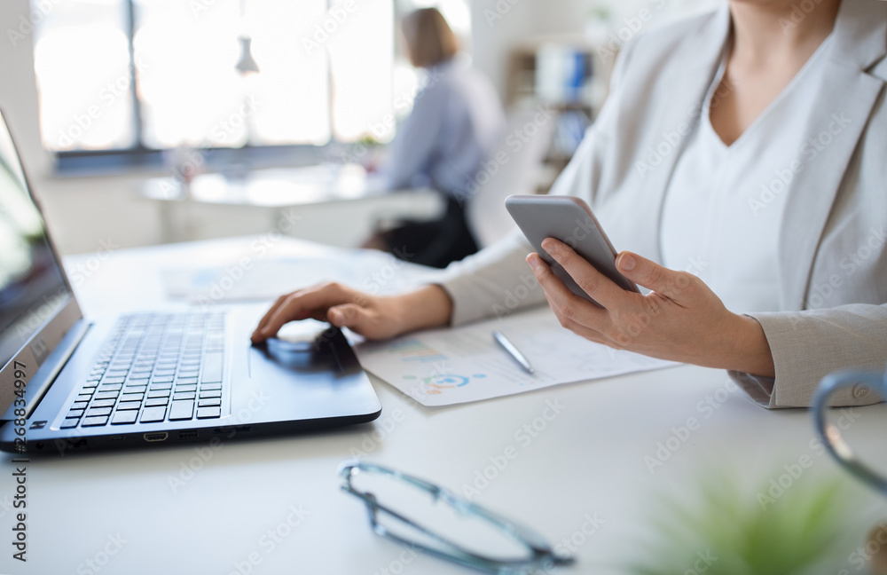 business, technology and people concept - businesswoman with smartphone and laptop computer at office