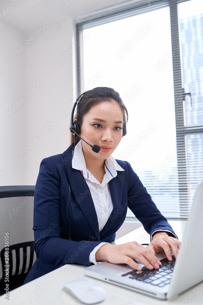Portrait of happy smiling female customer support phone operator at workplace. Asian Portrait of happy smiling female customer support phone operator at workplace. Asian