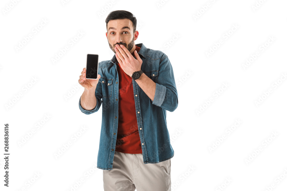 surprised bearded man covering mouth with hand while holding smartphone with blank screen isolated on white
