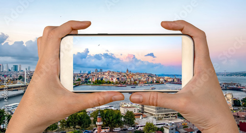 Travel concept - tourist taking photo of Golden Horn against Galata tower, Istanbul, on mobile gadget, Turkey