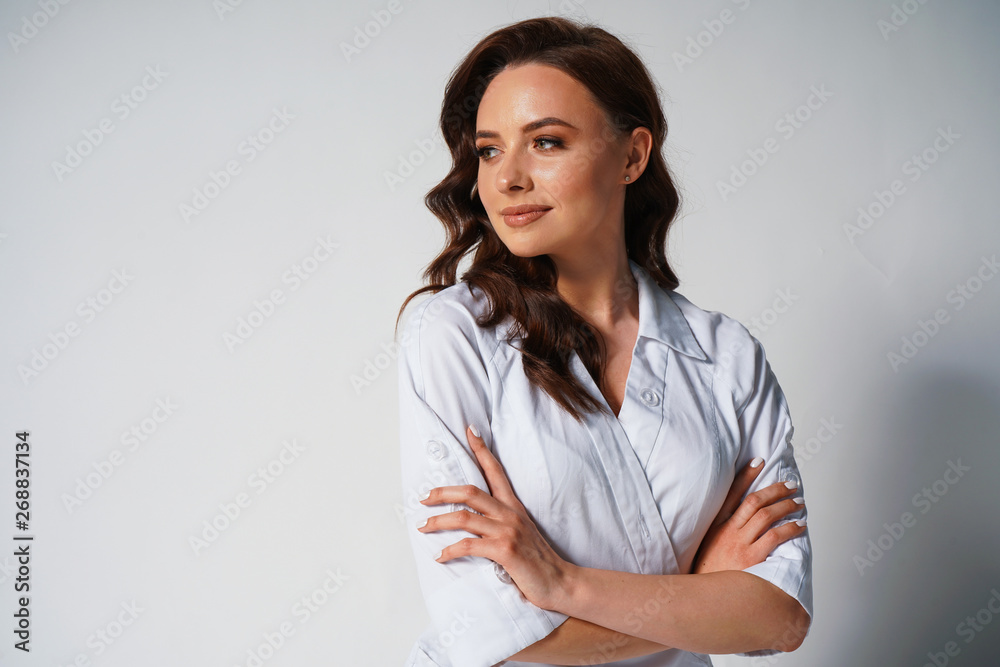 Portrait of beautiful young female doctor in white medical jacket isolated on white background. Brunette woman cosmetologist with cross hands. Copy space. Medical concept. Healthcare Portrait of beautiful young female doctor in white medical jacket isolated on white background. Brunette woman cosmetologist with cross hands. Copy space. Medical concept. Healthcare